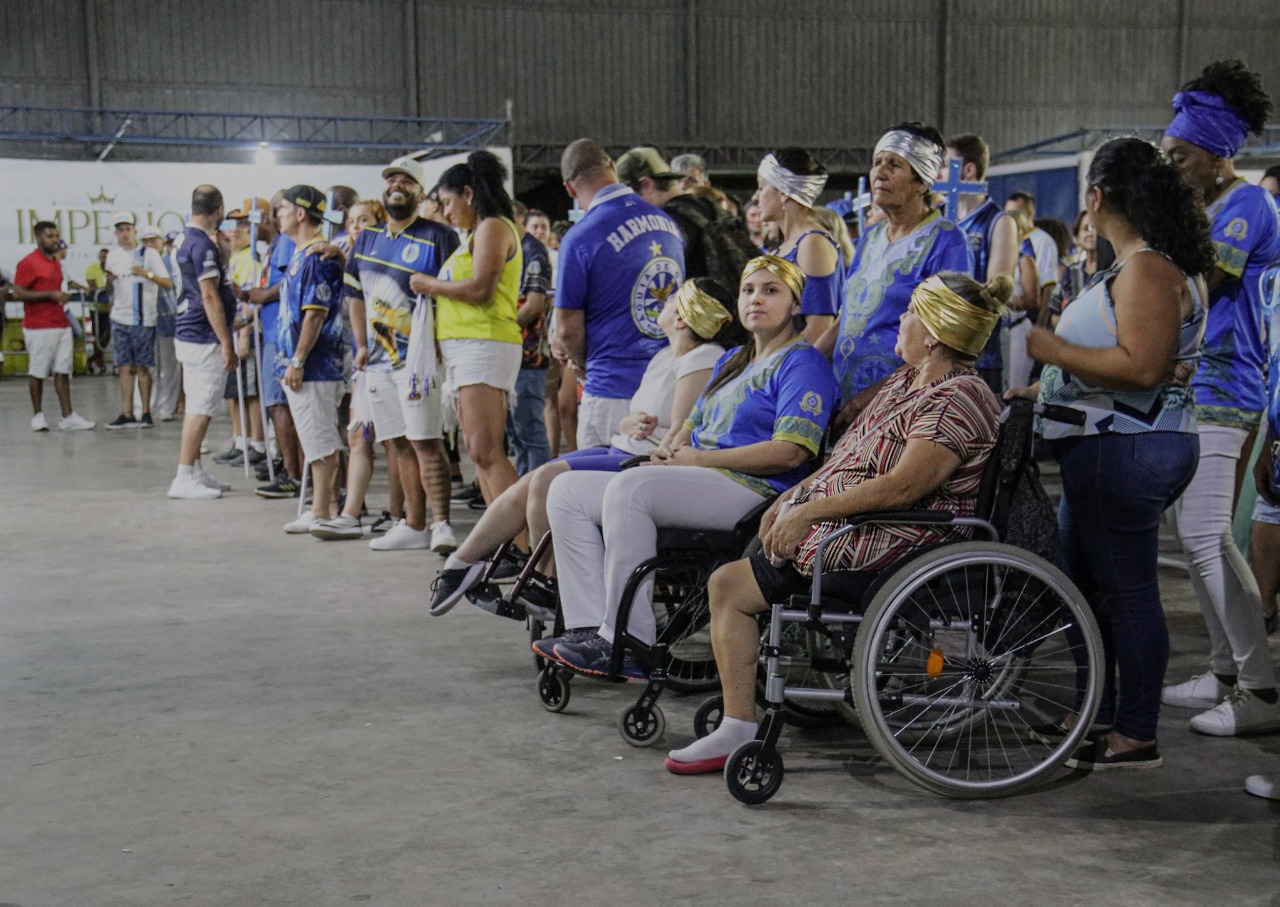 Na foto, na quadra da escola Águia de Ouro, é possível ver integrantes da escola entre eles, em destaque, há três mulheres que usam cadeira de rodas. Todos assistem a apresentação do Samba com as Mãos.